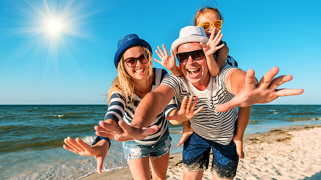 Rozbawiona trzyosobowa rodzina podczas pobytu na plaży w słoneczny dzień.